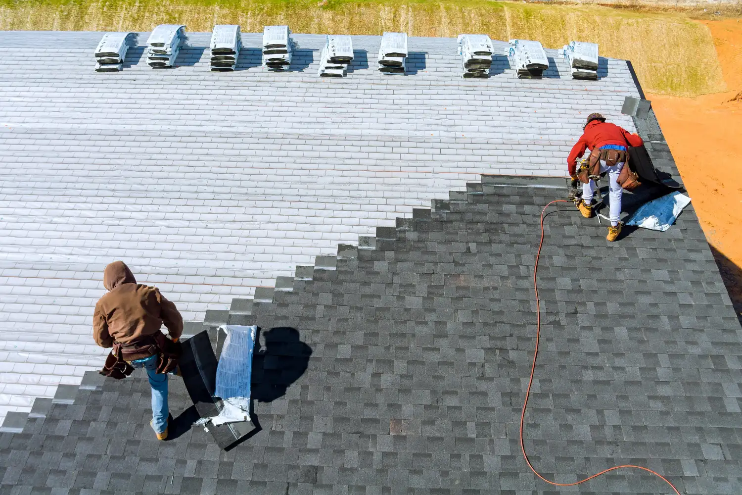 Roofers working on a shingled roof, seen from above